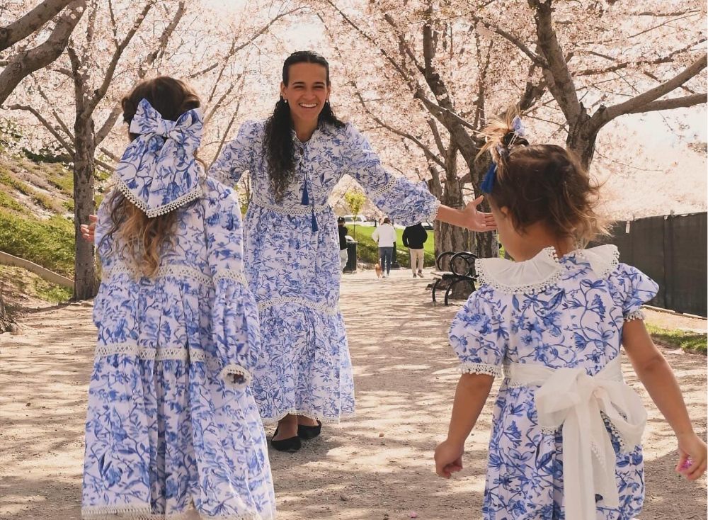 Two women and two children in matching blue and white floral outfits standing under cherry blossom trees.