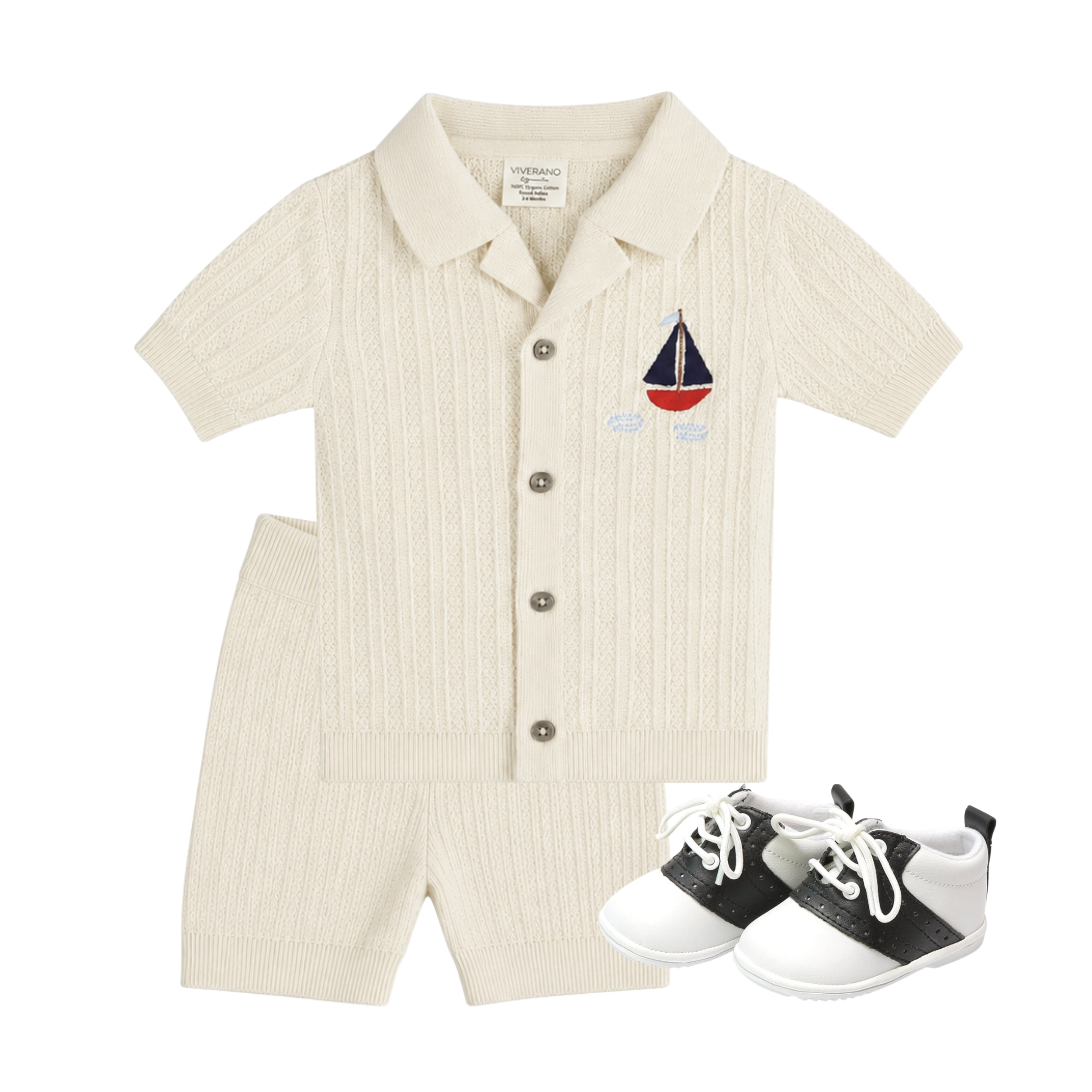 A baby boy's two-piece knit romper set in cream, featuring a short-sleeve button-front top with a small embroidered sailboat on the chest and matching shorts. A pair of black and white baby shoes is also included in the flat lay on a white background.