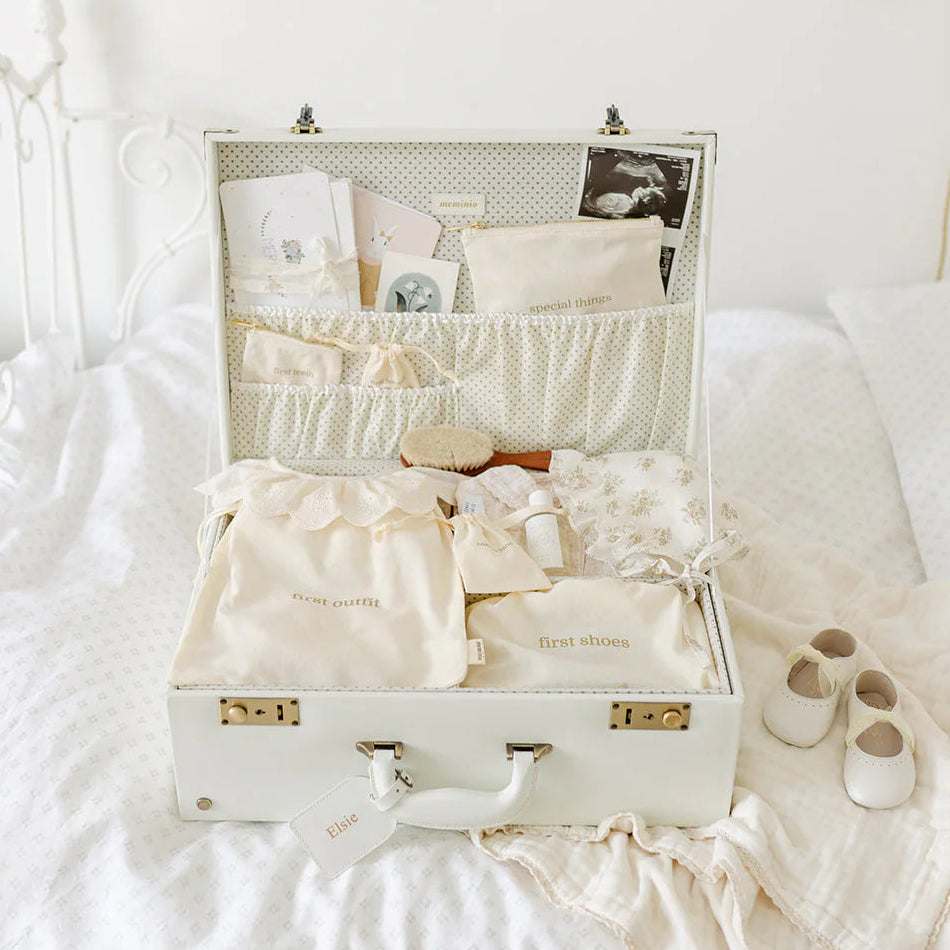 Open suitcase filled with baby clothes and items on a bed in a bedroom.