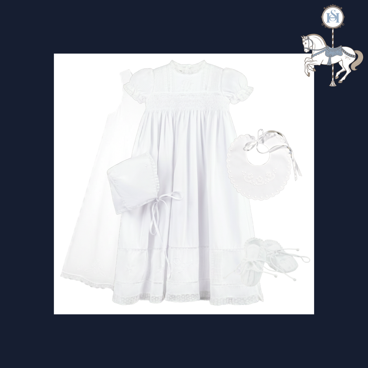A white baby girl's first christening outfit set featuring a smocked dress, matching veil, bib, pocket square, and booties, displayed on a white background with a dark navy border and a small carousel horse logo in the top right corner.