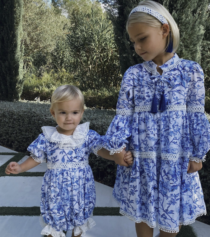 Two children in matching blue floral dresses standing outdoors.